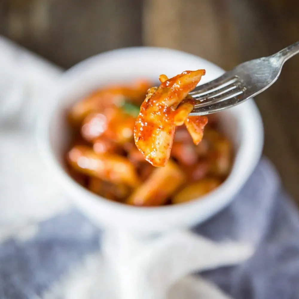 Close-up forkful of Tteokbokki Recipe rice cakes coated in vibrant red gochujang sauce.