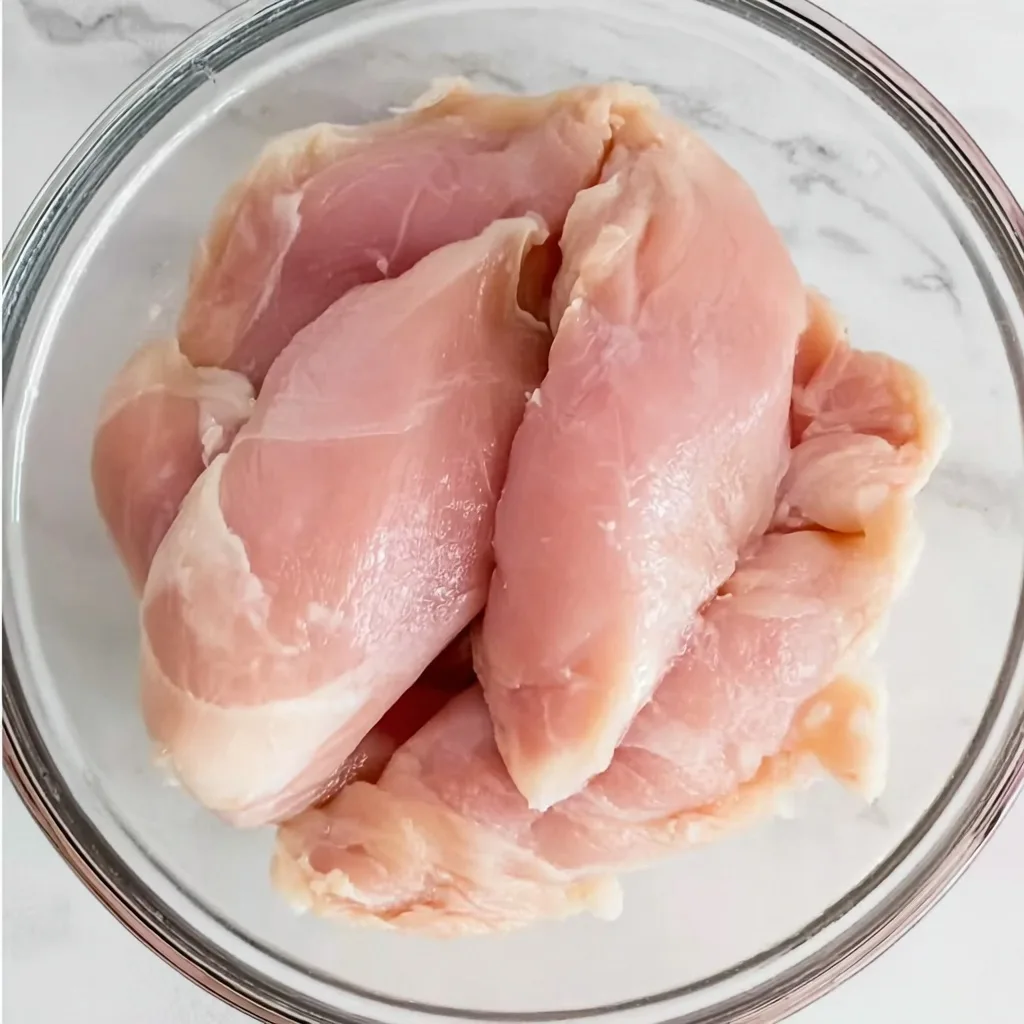 Raw chicken tenders placed in a clear glass bowl on a white marble countertop, ready for seasoning and air frying.