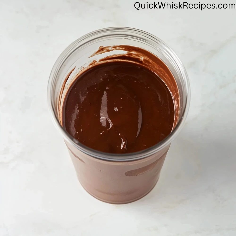 A thick, dark chocolate tofu pudding mixture in a clear blender cup placed on a white countertop.