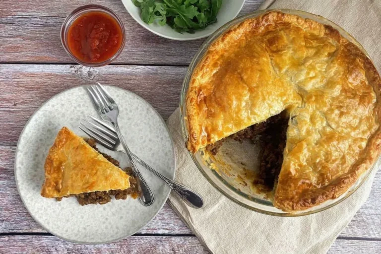 Golden-baked mince and cheese pie with a slice served on a plate beside tomato chutney and salad