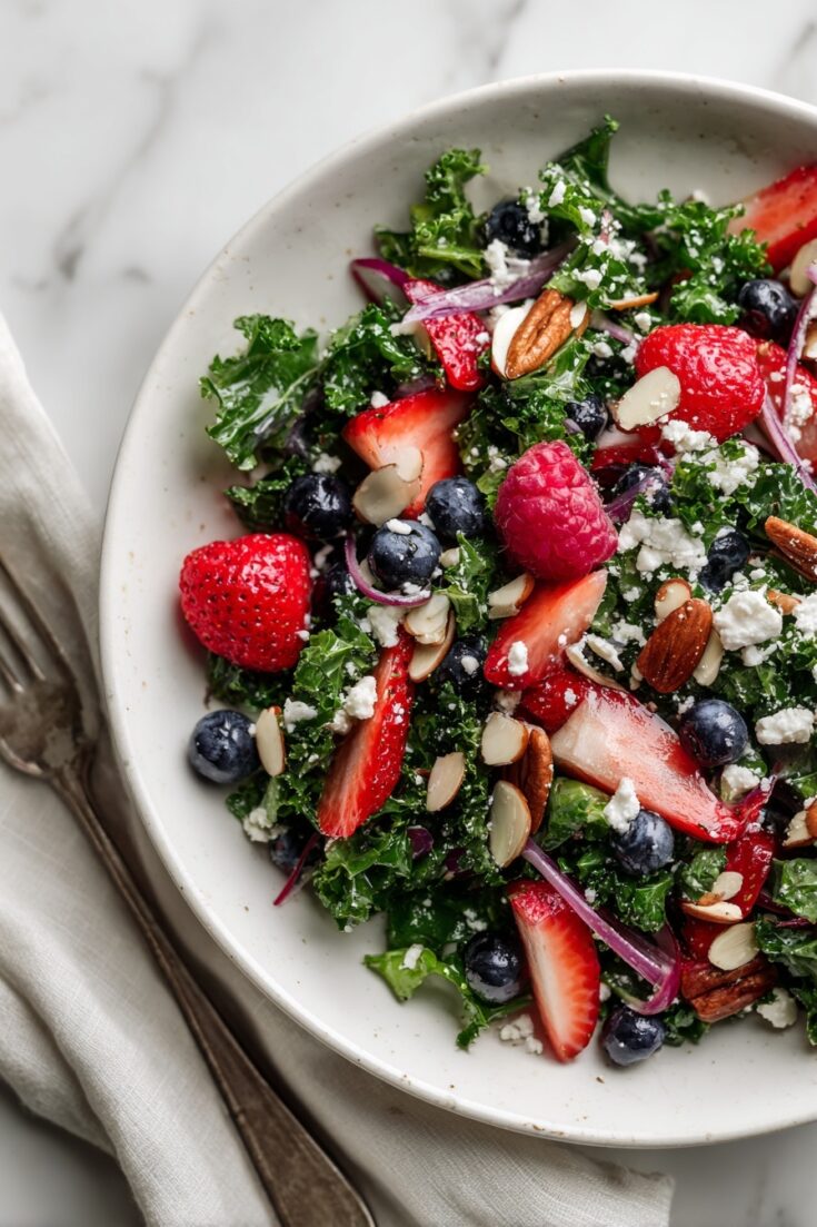 Finished kale salad with berries, feta, almonds, and fresh fruit served in a white bowl