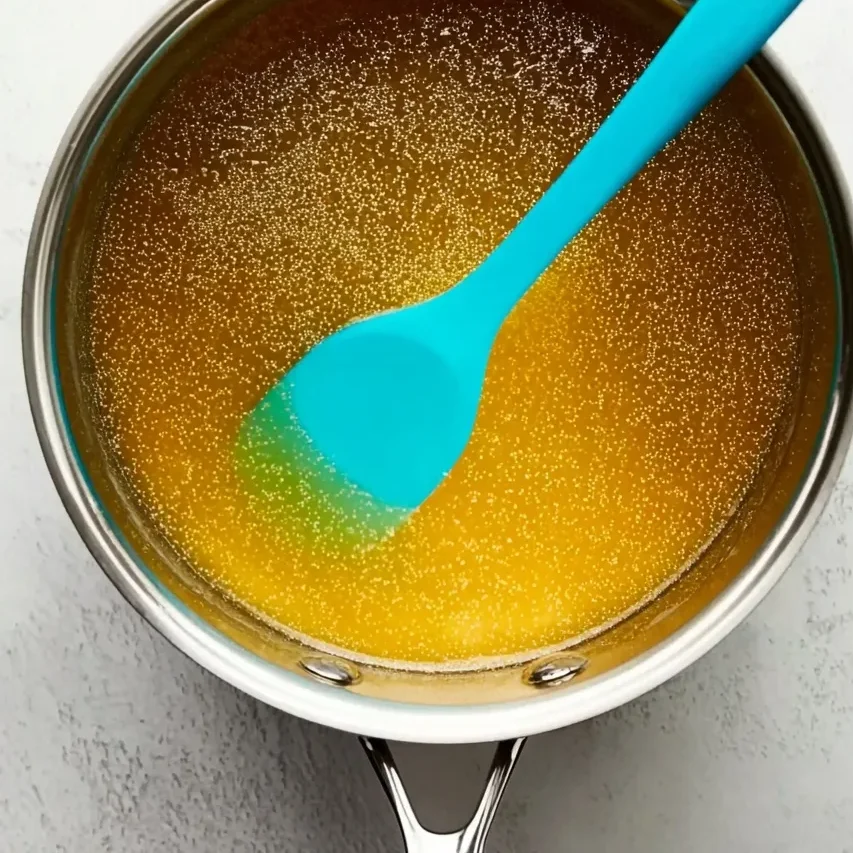 Melted butter and golden syrup bubbling gently in a saucepan with a blue silicone spoon