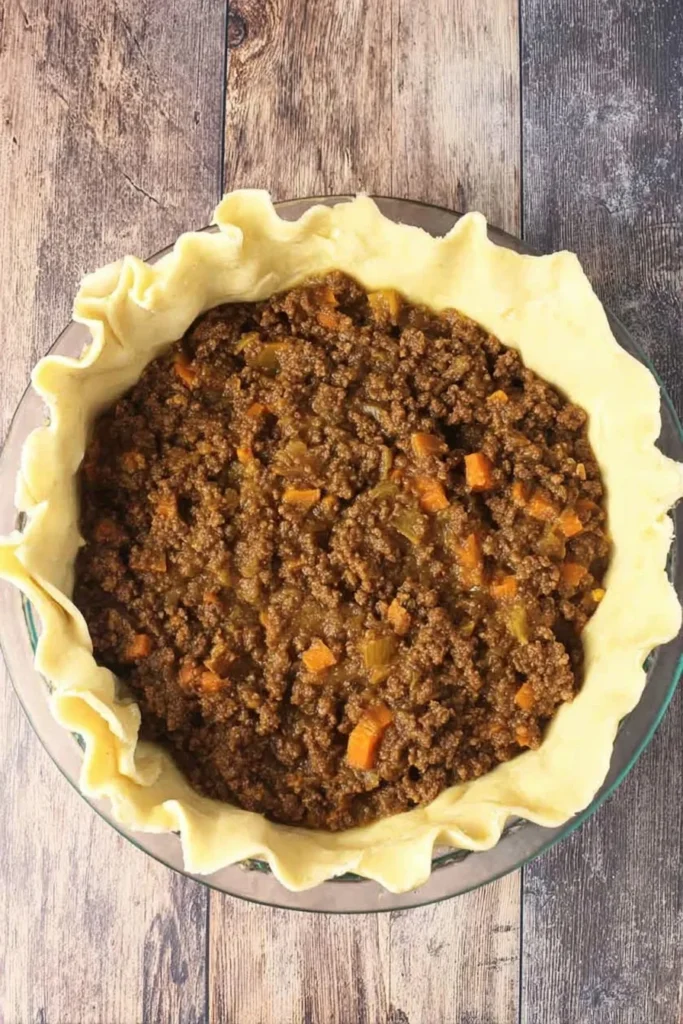 Unbaked pie shell filled with savory ground beef and diced vegetables, ready for cheese topping and crust