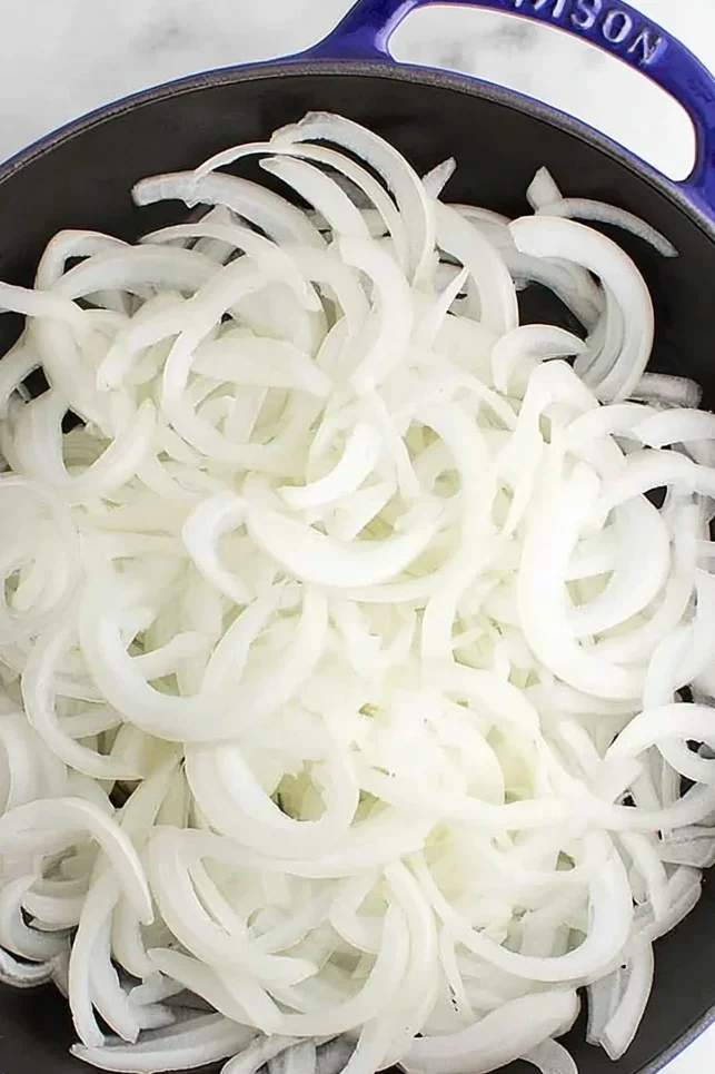 Raw sliced white onions in a cast iron skillet before caramelizing
