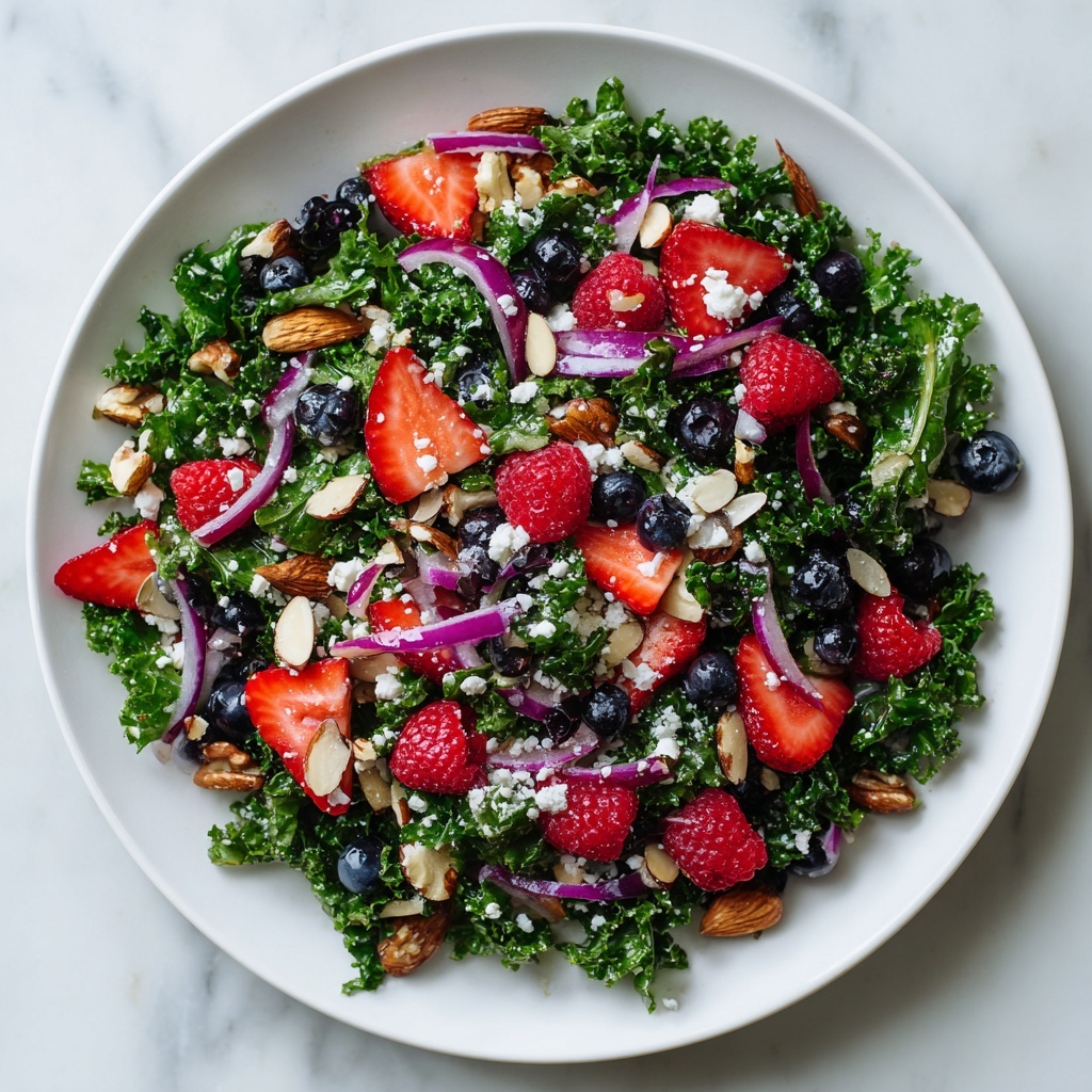 Kale salad with berries, almonds, feta, and red onion on white plate overhead