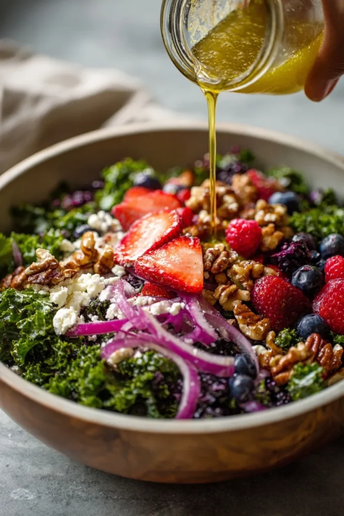 Pouring vinaigrette over kale salad with berries, walnuts, feta, and fresh fruit