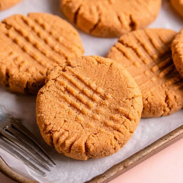 Close-up of freshly baked 3 ingredient peanut butter cookies with fork marks on top, cooling on a baking tray.