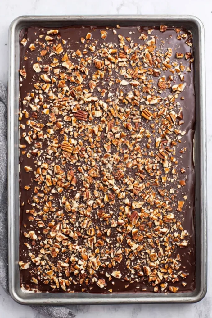 Christmas crack topped with melted chocolate and chopped pecans on a baking sheet