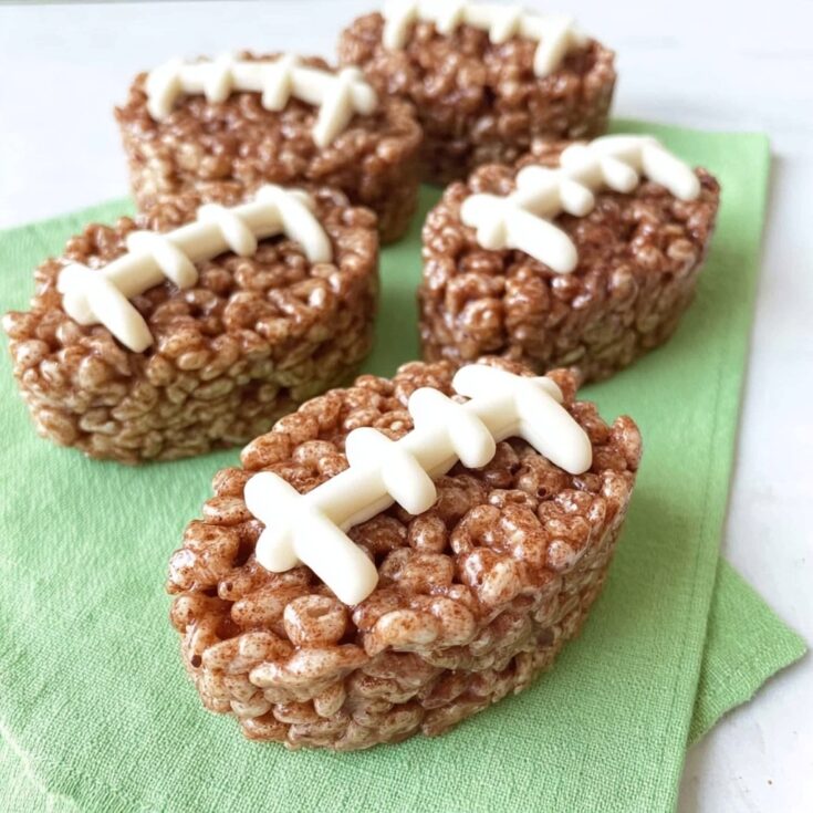 Close-up of football rice krispie treats on a green napkin, decorated with white icing laces for Super Bowl and game day desserts.