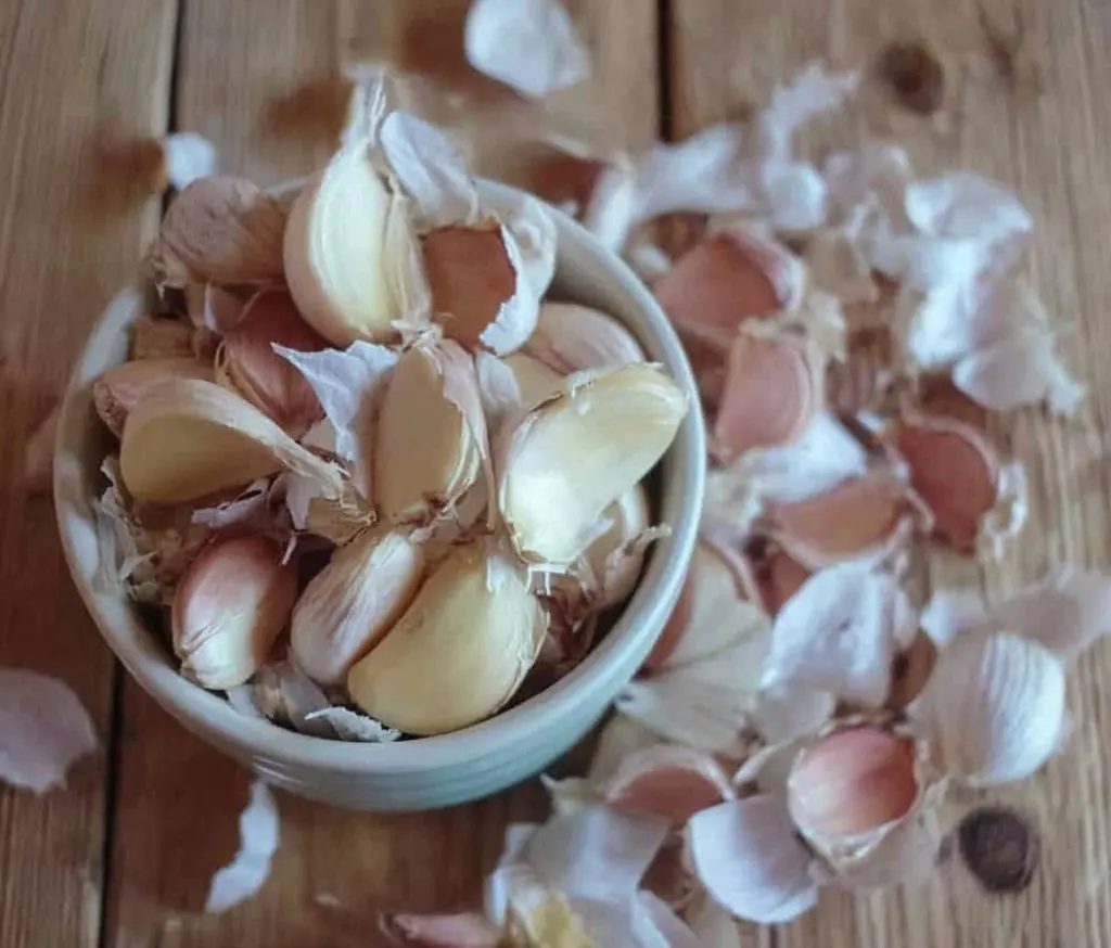 Bowl of fresh garlic cloves with skins partially peeled, ready to be used for homemade pickled garlic.