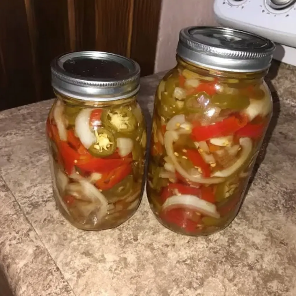 Two mason jars filled with pickled jalapenos, onions, and red peppers on a kitchen counter
