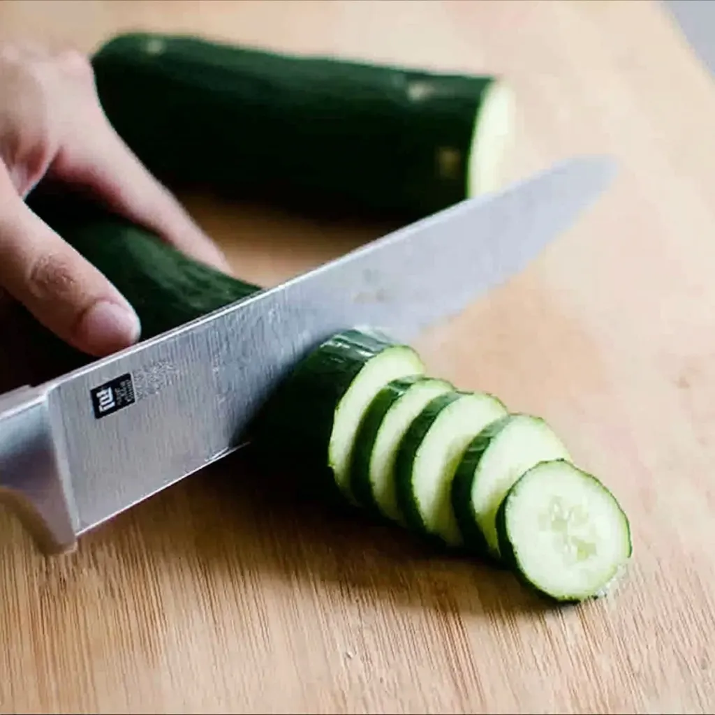 Hand slicing fresh cucumbers on a wooden board to prepare easy refrigerator pickles