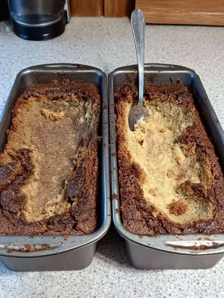 Two loaf pans with collapsed zucchini bread showing raw, underbaked centers and overbrowned edges, with a spoon in one loaf.