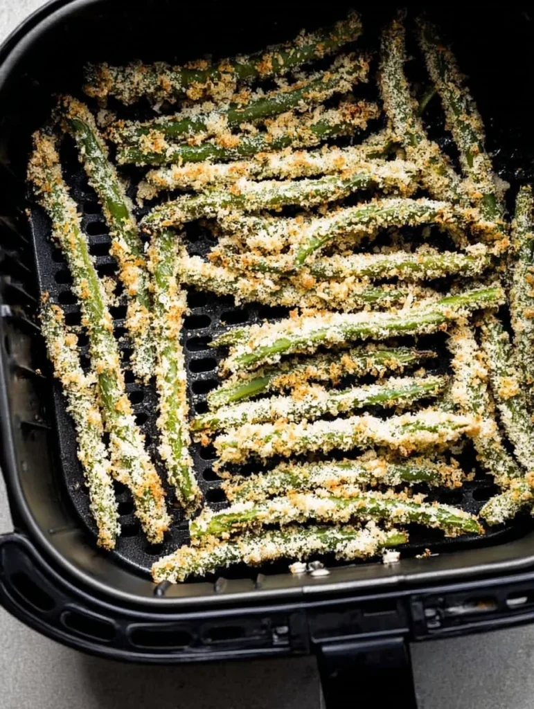 Breaded green beans arranged in an air fryer basket before cooking until crispy.