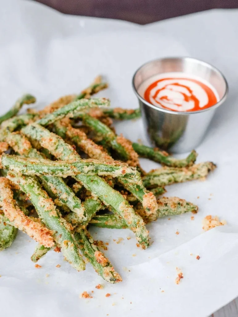 Crispy air fryer green bean fries served with dipping sauce on parchment paper.
