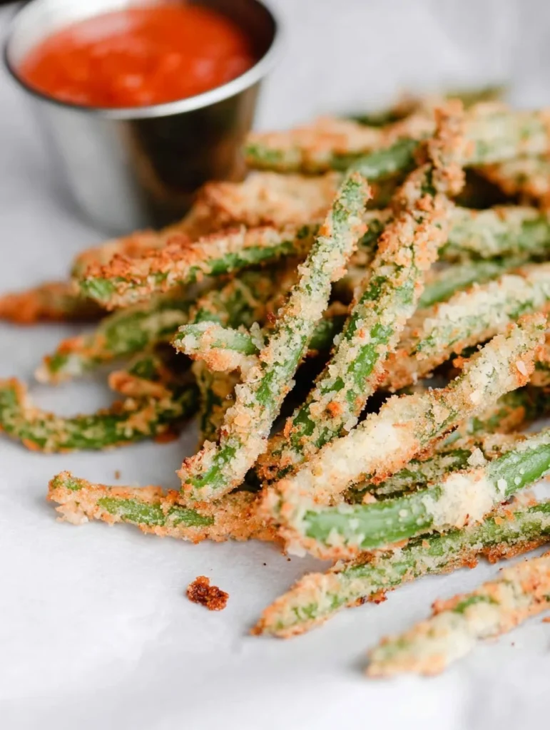 Close-up of crispy air fryer green bean fries with a cup of spicy dipping sauce.