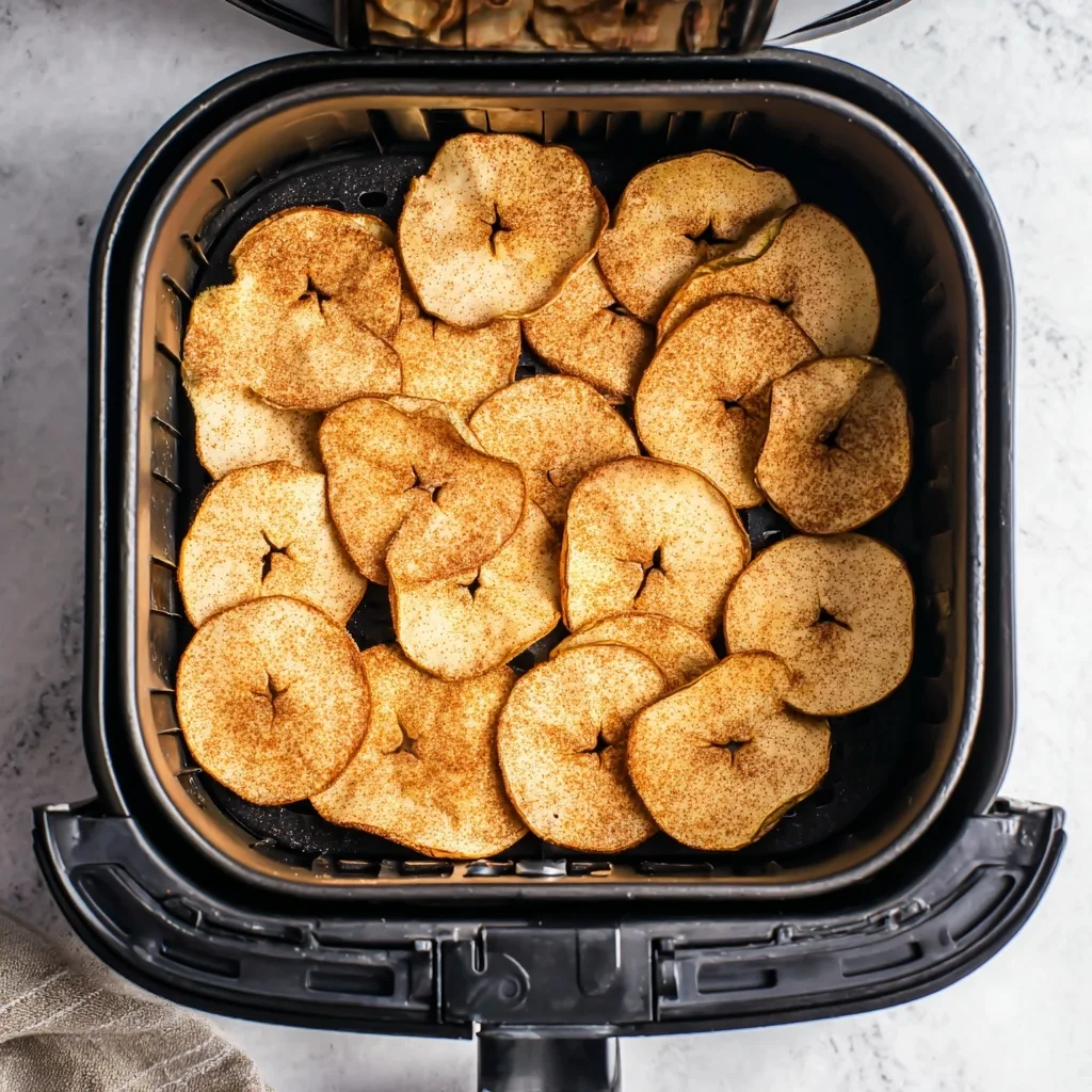 Thin apple slices arranged in an air fryer basket before cooking