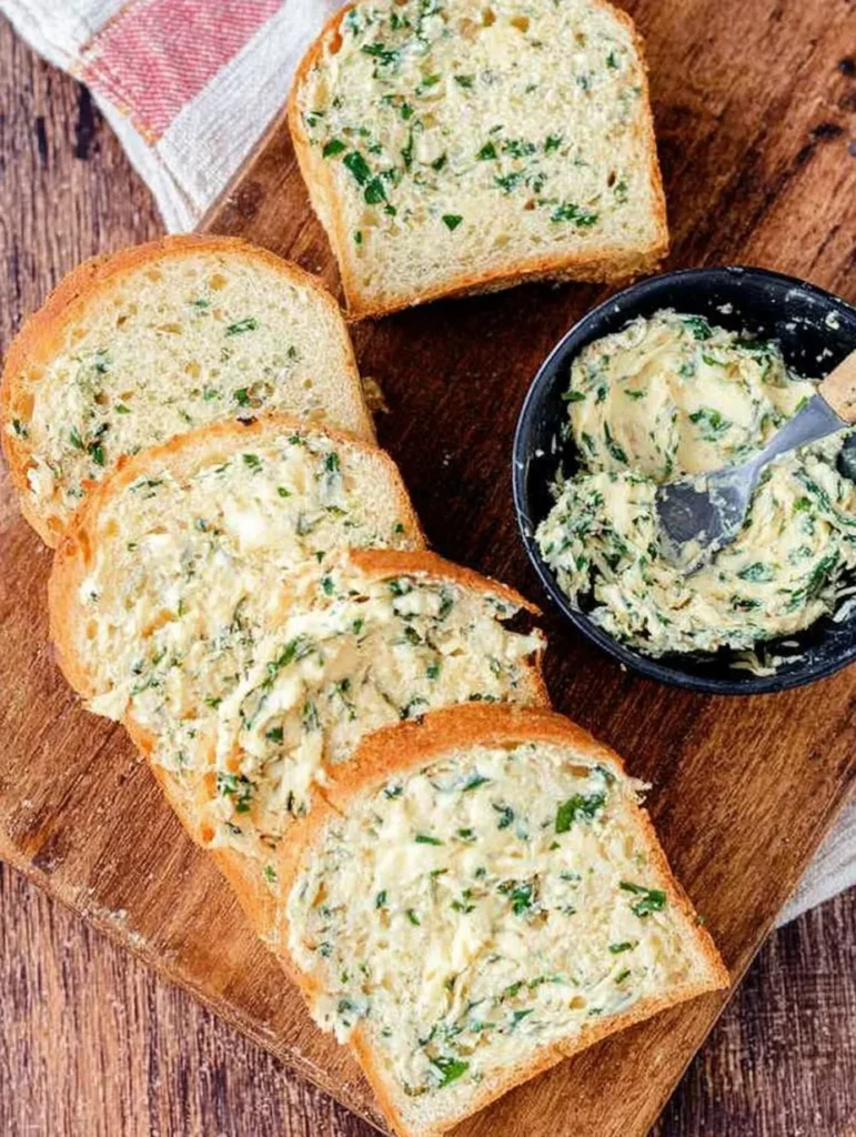 Slices of bread spread with fresh garlic butter and parsley on a wooden board