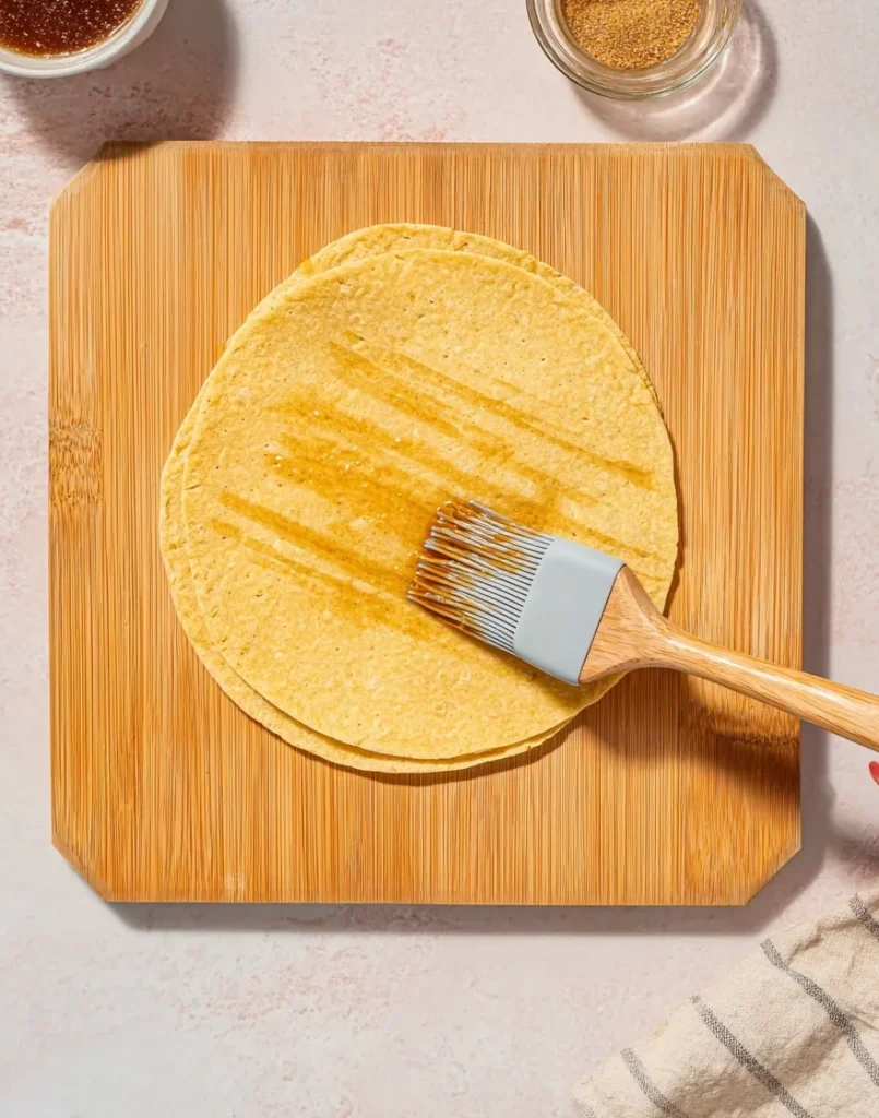 Corn tortilla being brushed with oil and seasoning on a wooden board before air frying