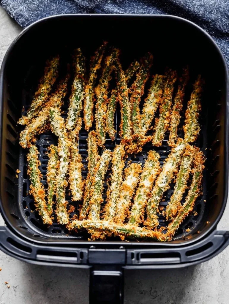 Golden and crispy air fryer green bean fries in the basket after cooking.