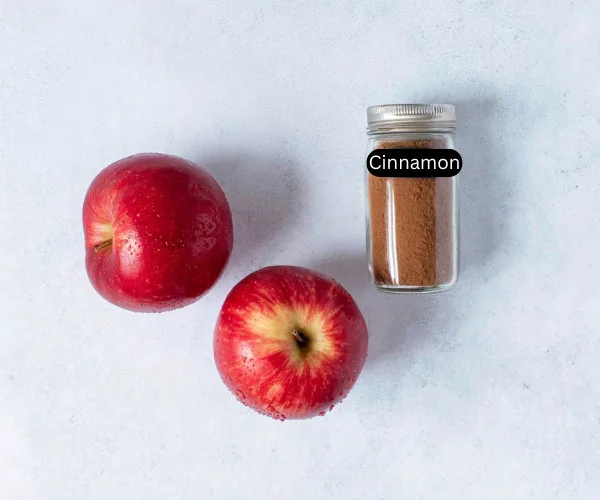 Two fresh red apples with a jar of ground cinnamon