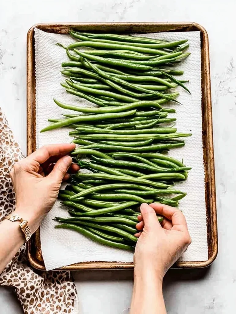 Hands arranging fresh green beans on a tray lined with paper towels before cooking.