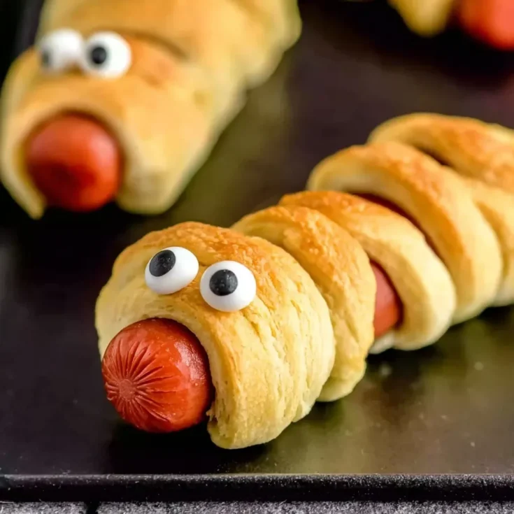 Close-up of a hot dog wrapped in crescent roll dough with candy eyes, styled as a Halloween mummy.
