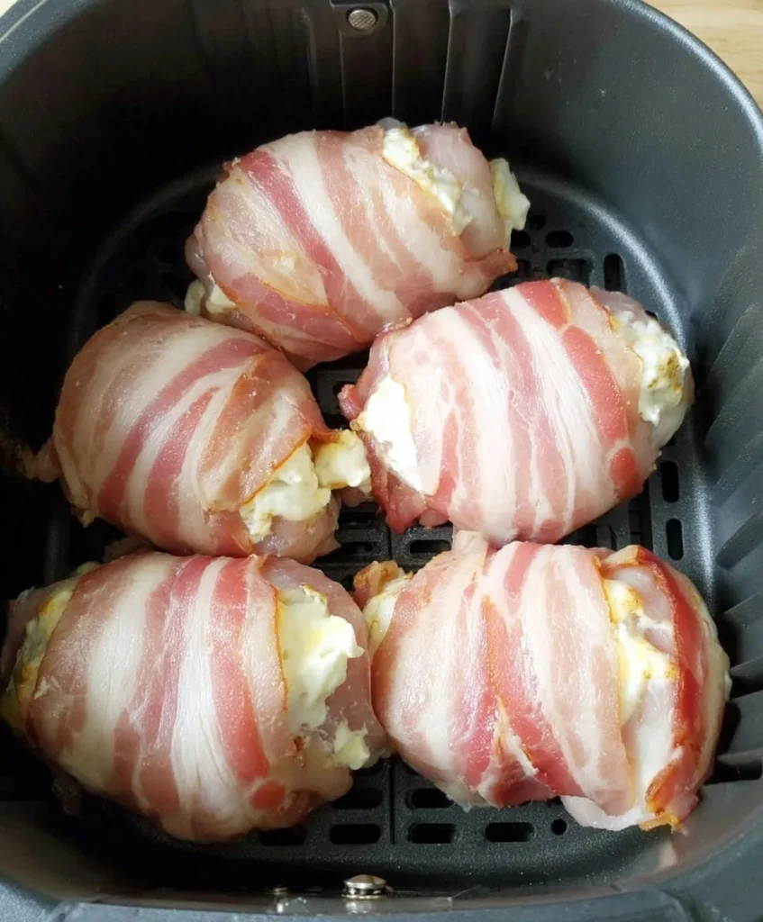 Raw bacon wrapped jalapeño popper chicken stuffed with cheese arranged in an air fryer basket before cooking