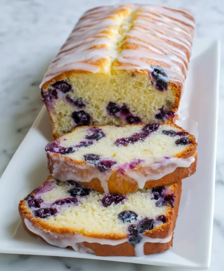 Moist blueberry lemon pound cake topped with lemon glaze and sliced on a white plate.