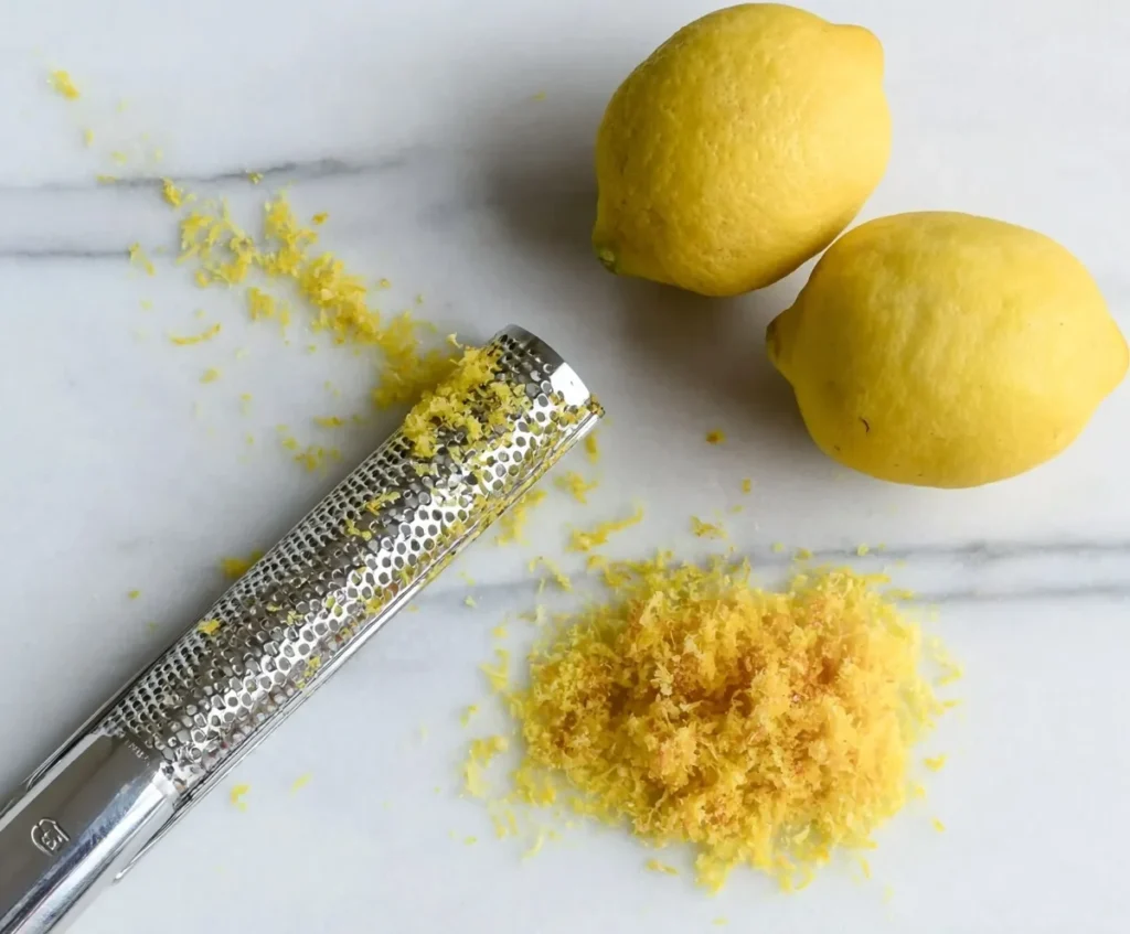 Fresh lemons with zest and a grater on marble surface for blueberry lemon pound cake recipe.