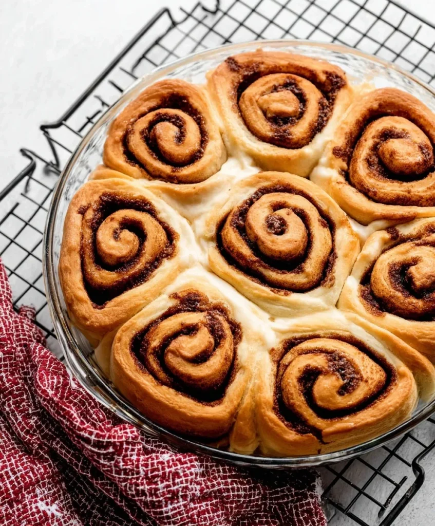 Golden brown cinnamon rolls fresh from the oven in a glass baking dish on a cooling rack.