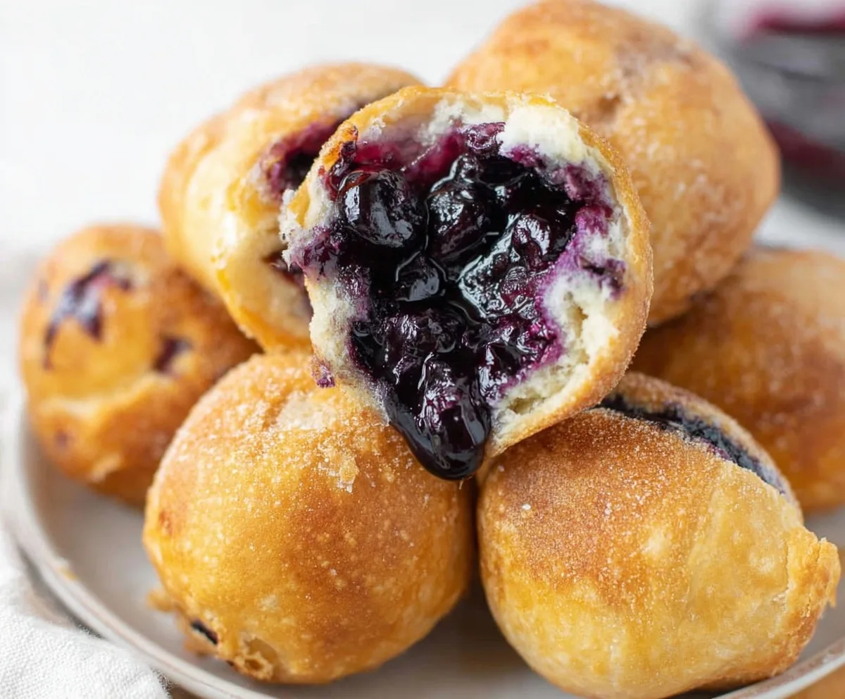 Close-up of warm golden pastries filled with juicy blueberry filling stacked on a plate.