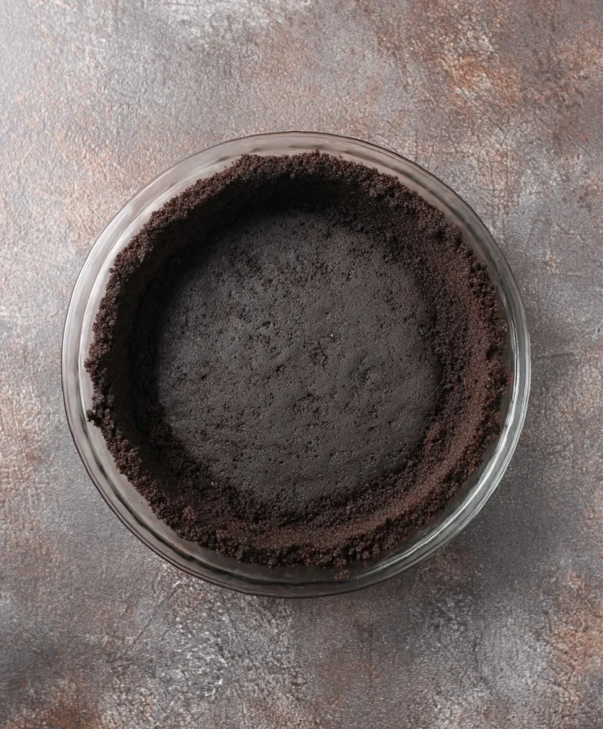 Empty Oreo cookie crust pressed into a glass pie dish ready for chocolate cream pie filling.