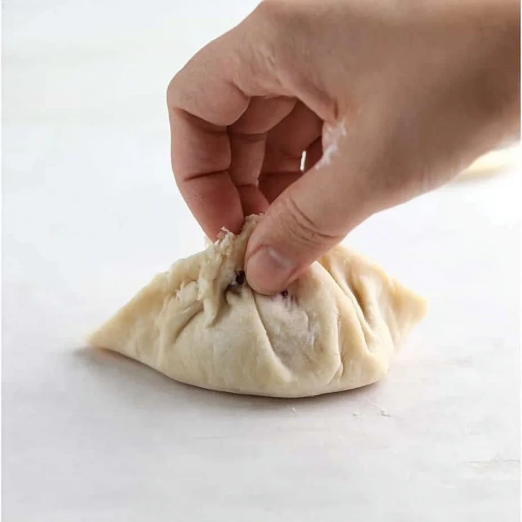 Hand sealing biscuit dough around blueberry filling to form small dessert pastries.