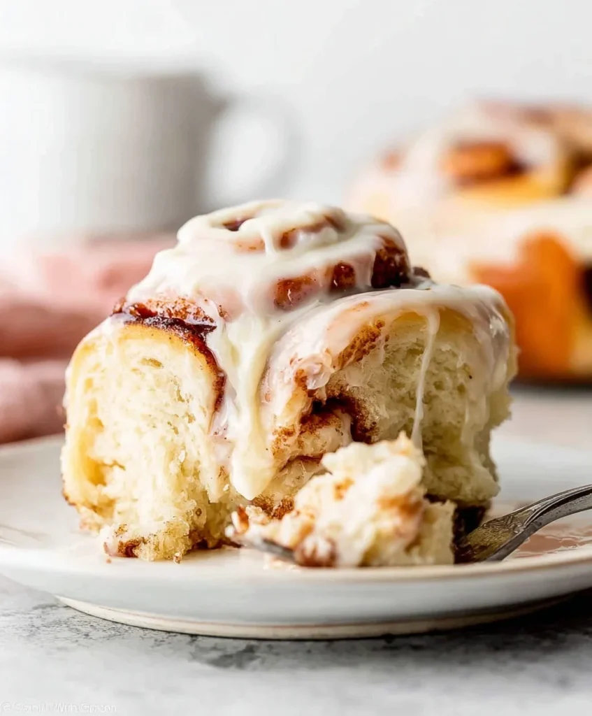 Soft, gooey homemade cinnamon roll topped with creamy glaze on a white plate.