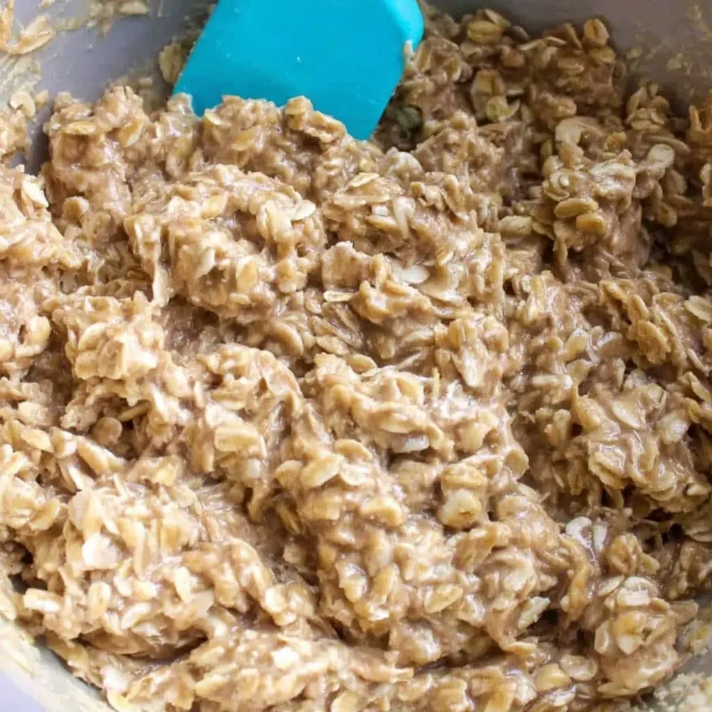 Close-up of sugar free oat biscuit dough being mixed in a bowl with a blue spatula.