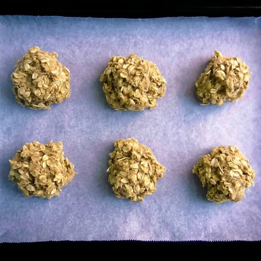 Scoops of sugar free oat biscuit dough placed on parchment paper ready for baking.