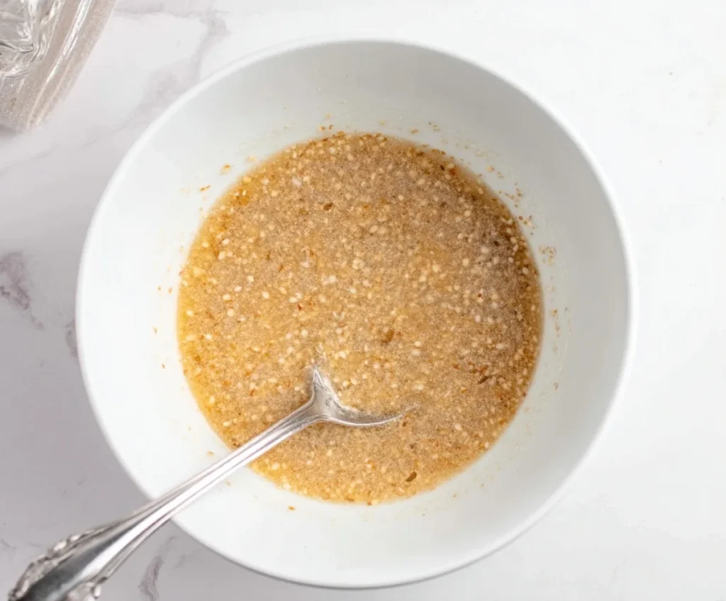 Wet ingredients for sugar free oat biscuits mixed in a white bowl with a silver spoon.