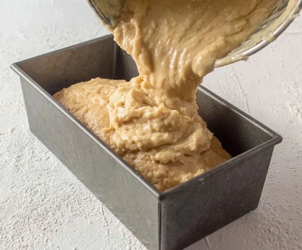 Banana bread batter being poured into a loaf pan before baking.