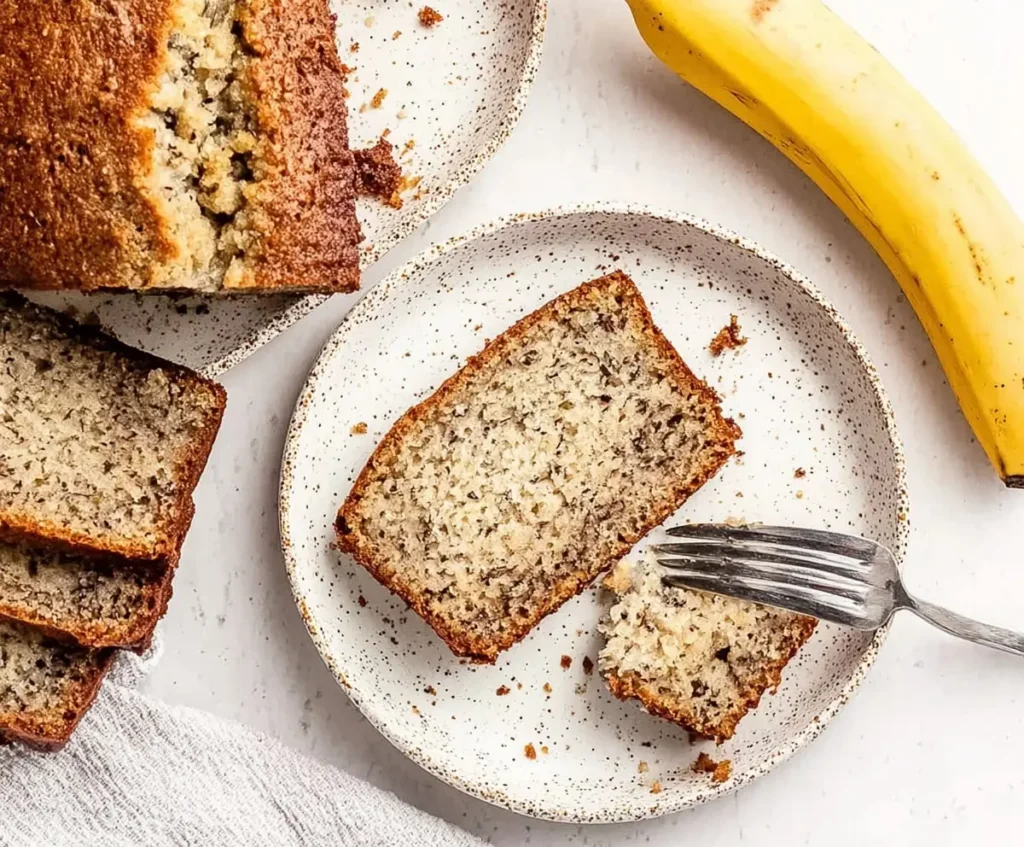 Sliced banana bread served on small plates with a fork and a fresh banana on the side.