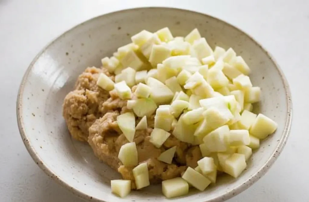Bowl filled with diced apples and muffin batter, ready to mix.
