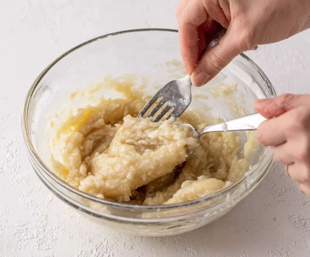 Mashing ripe bananas in a glass bowl for banana bread.