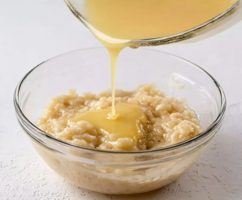 Pouring melted butter into a bowl of mashed bananas.