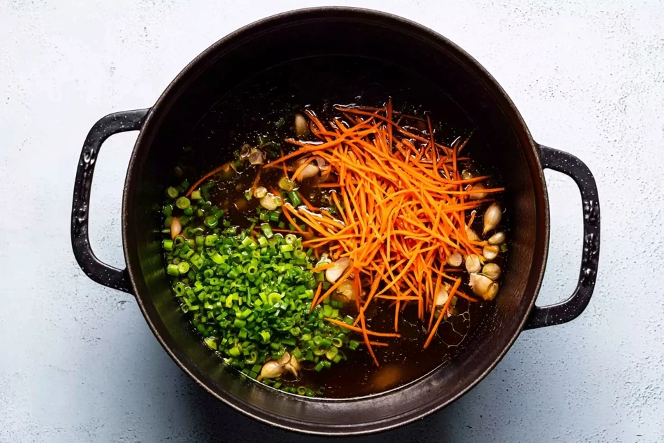 Julienned carrots, chopped green onions, and garlic cooking in a pot as the base for dumpling soup