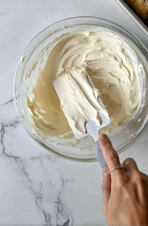 Cream cheese frosting being mixed in a bowl for cranberry bliss bars, with baked bars in the background