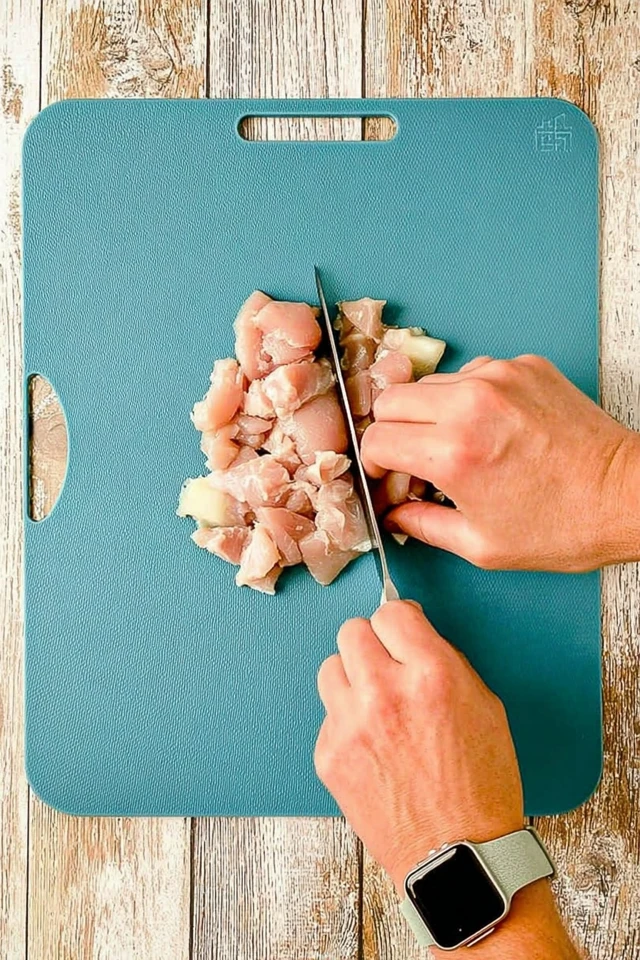 Cutting raw chicken into bite-size pieces on a cutting board