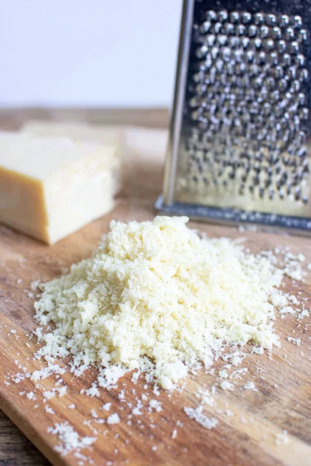 Freshly grated parmesan cheese on a wooden board with a cheese grater and parmesan block