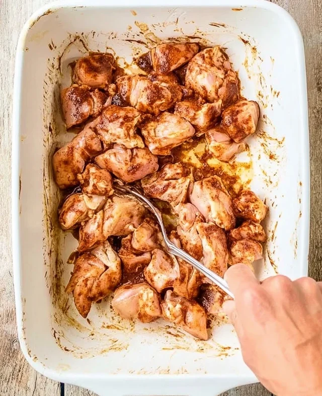 Mixing seasoned chicken pieces in a baking dish before baking