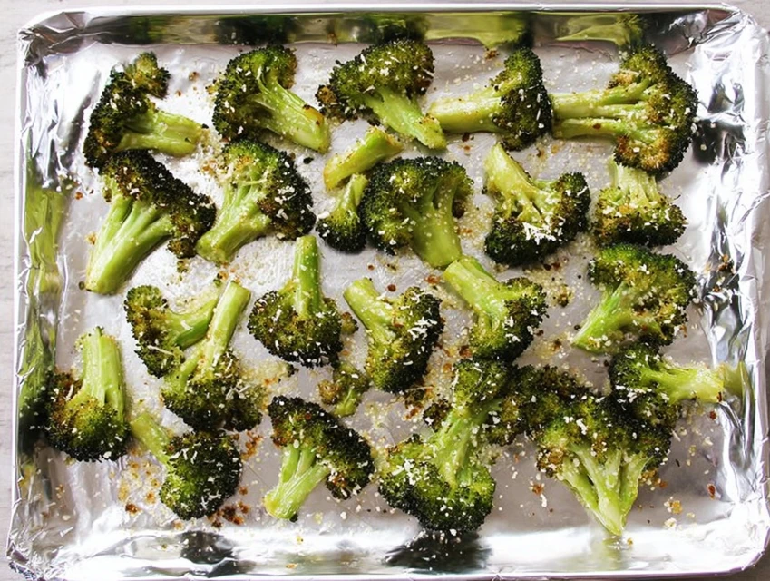 Broccoli florets roasting on a foil-lined baking sheet with parmesan cheese, evenly spaced for crispy oven roasting