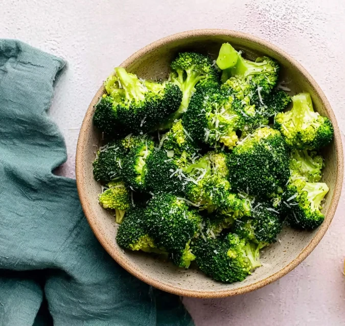 Raw broccoli florets in a bowl, lightly sprinkled with grated parmesan cheese before roasting
